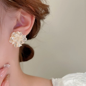 Detail shot of a floral earring featuring pearlescent petals and embedded crystals