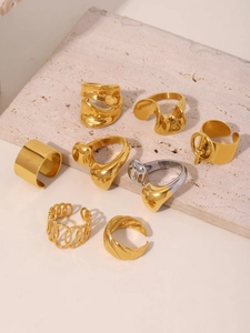 Set of eight gold PVD plated stainless steel rings on a beige stone surface