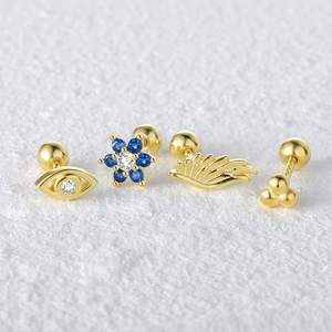 Macro shot of gold S925 sterling silver piercing studs with blue flower and eye designs