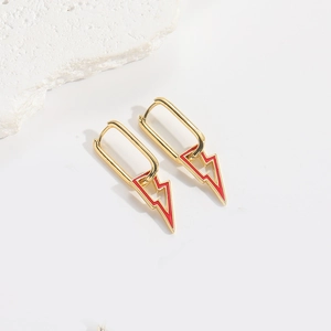 Detailed close-up of gold rectangular earrings with red lightning pendants on white stone