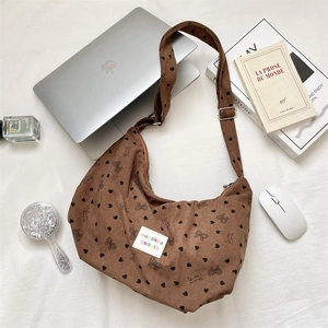 Brown corduroy crossbody bag with heart bow prints next to a laptop and books