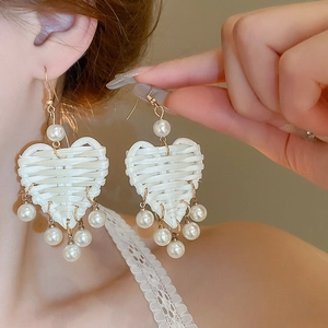 Détail de boucles d'oreilles cœur tressées à la main avec perles et touches dorées