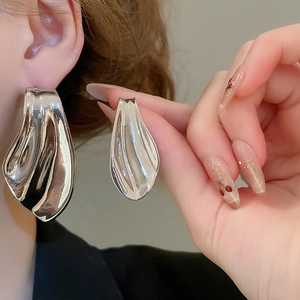 Close-up of asymmetric silver fish-tail earring with polished metallic mirror finish