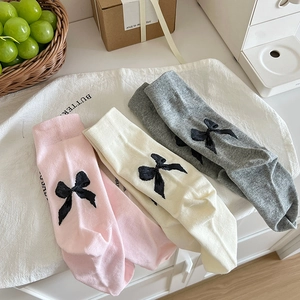 Detailed view of grey, pink, and off-white lace socks with black bows on white fabric