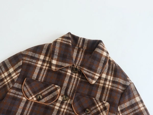 Detail of plaid jacket collar, front buttons, and chest pockets with brown piping trim