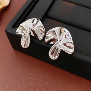 Macro shot of silver sculptural earrings with flowing metal texture on a black jewelry box