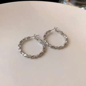 Detailed close-up of silver minimalist earrings with irregular faceted texture on ceramic