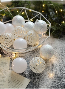 Detail view of white Christmas balls with glitter, matte, and cutout patterns in a basket