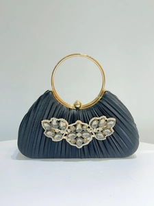 Detail of elegant black pleated satin clutch with floral crystal cluster and gold ring handle