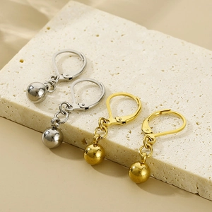 Close-up of polished gold and silver ball drop earrings on beige textured stone surface