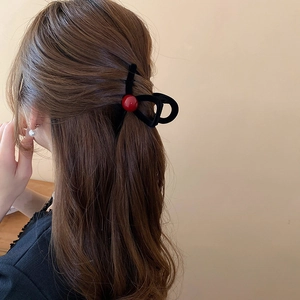 Detail of a black velvet hair claw clip with a red bead accent on brown wavy hair