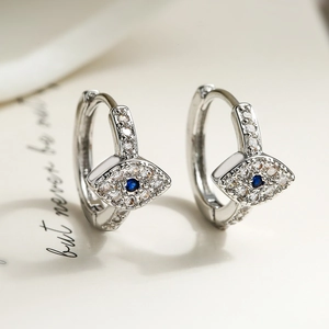 Silberne Creolen mit bösem Blick, blauem Zirkon und Pavé-Steinen auf beiger Karte