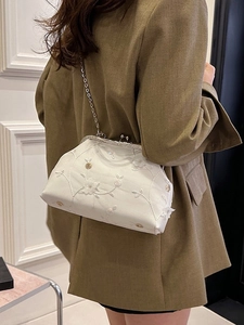 Elegant white embroidered floral frame bag with metal chain strap shown on a model side view