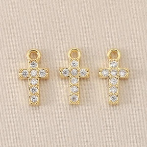 Three baroque gold-plated cross pendants with clear rhinestones on beige fabric