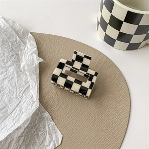 Close-up of checkerboard hair claw clip on a beige leather mat with elegant lighting