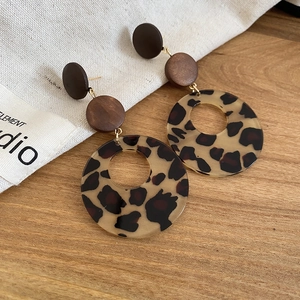 Macro shot of leopard print resin and dark wood geometric hoop earrings on a wooden table