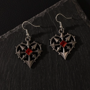 Macro shot of gothic thorn heart earrings with red crystal on black rock background