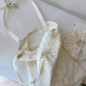Detailed macro view of cream cotton tote bag with white polka dot jacquard texture and scrunchie