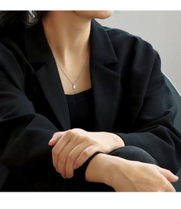 Close-up of minimalist silver oval pendant necklace on a model wearing a black blazer