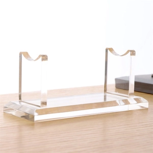 Clear acrylic pen and sword display stand with dual U-shaped brackets on a wood desk