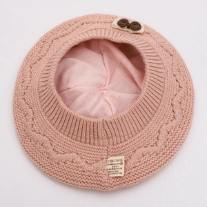 Detailed macro of pink knit beret featuring cable texture and washing care label