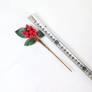 Close-up of artificial red berry stem with green leaves measuring 20cm on marble background