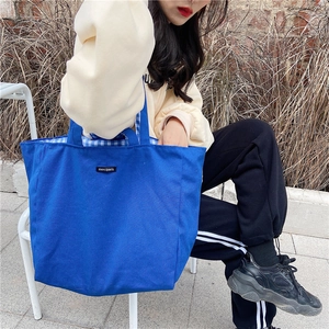 Outdoor shot of blue canvas tote bag with inner checkerboard lining and logo detail