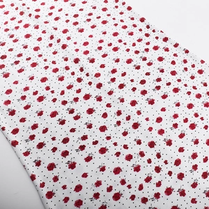 Detalle de tela floral con pequeñas rosas rojas y lunares negros sobre un fondo blanco