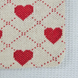 Close-up of knit fabric texture with red heart pattern on a creamy beige tote bag