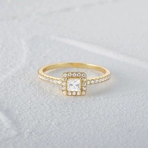 Macro shot of square-cut diamond halo ring in gold finish on white stone texture