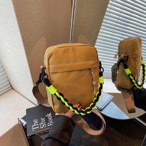 Detail of khaki canvas shoulder bag featuring a neon green woven handle and zipper