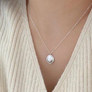 Detail of round silver pendant necklace worn over a soft cream knit sweater texture