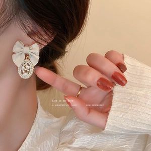 Elegant beige fabric bow earrings with oval pearl and rhinestone charms shown on a model