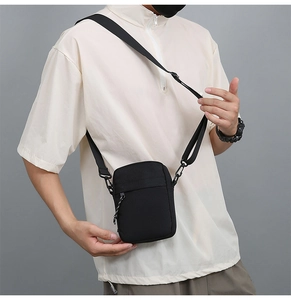 Detail of compact black nylon shoulder bag showing zipper pocket and adjustable strap
