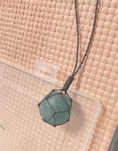 Vue détaillée d'une pierre brute vert clair fixée par un filet noir tressé à la main