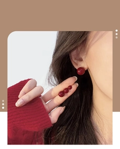 Detail of deep red spherical stud earrings in various sizes shown on a model
