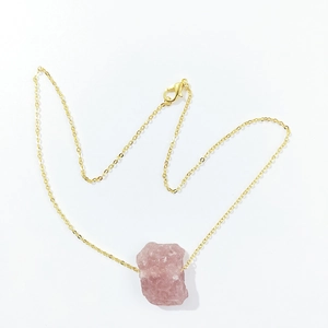 Detail shot of irregular pink natural raw stone pendant on a delicate gold link chain