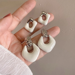 Detail view of two pairs of geometric enamel silver earrings in hand with beige backdrop
