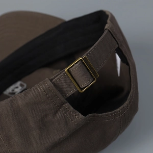 Detail of adjustable metal buckle and stitching on dark brown cotton baseball cap