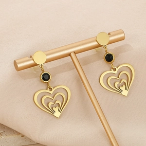 Détail de boucles d'oreilles cœur en acier titane doré avec pierre noire sur socle