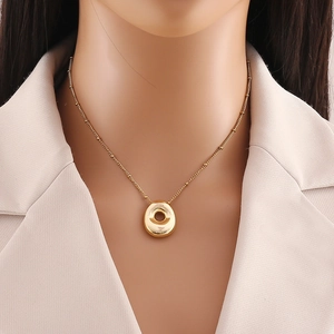 Dettaglio del ciondolo circolare placcato oro 18K con catena a sfere su collo di modella