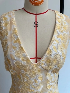 Detailed close-up of V-neck white lace dress with floral patterns and gold sequins
