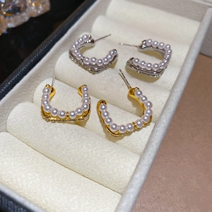 Macro detail of U-shaped gold and silver pearl earrings with sparkling zircon accents