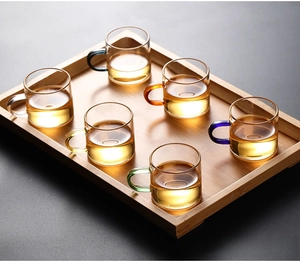 Detailed view of six heat-resistant glass tea cups with colorful handles on wooden tray