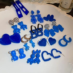 Detail of blue flocked teddy bear and heart stud earrings collection on ceramic tray
