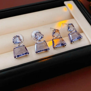 Close-up of geometric silver earrings with purple crystals in a black jewelry box