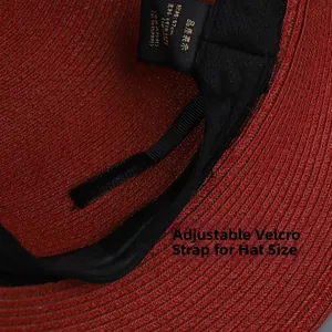Detail view of the red straw hat featuring a black adjustable velcro strap for custom fit