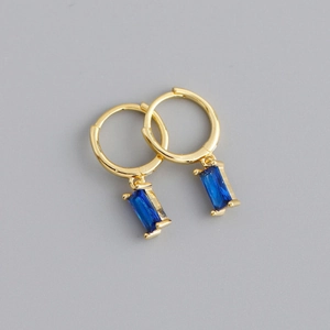 Dettaglio di orecchini huggie dorati con eleganti ciondoli rettangolari in gemma blu