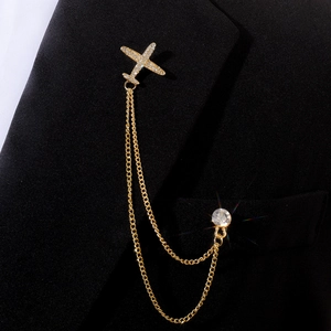 Détail d'une broche avion dorée avec double chaîne et strass sur revers de veste noir