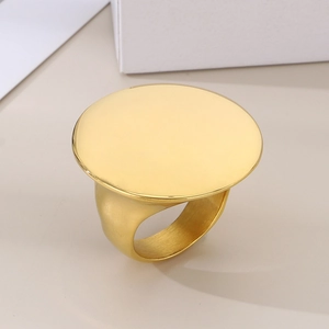 Close-up of a bold 18k gold plated stainless steel flat round disk ring on beige surface